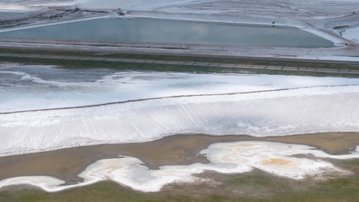 Aerial view of lithium brine ponds with white salt deposits and a turquoise evaporation pool in open terrain